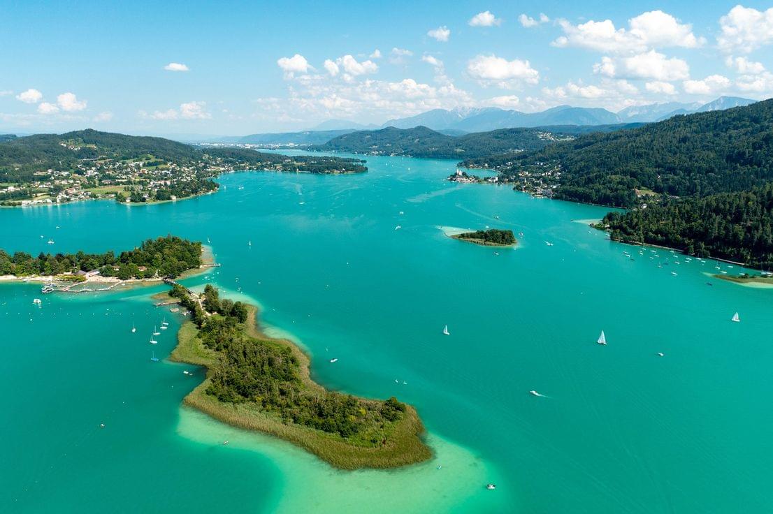 Luftaufnahme vom türkisfarbenen Wörthersee mit Segelbooten und bewaldetem Ufer